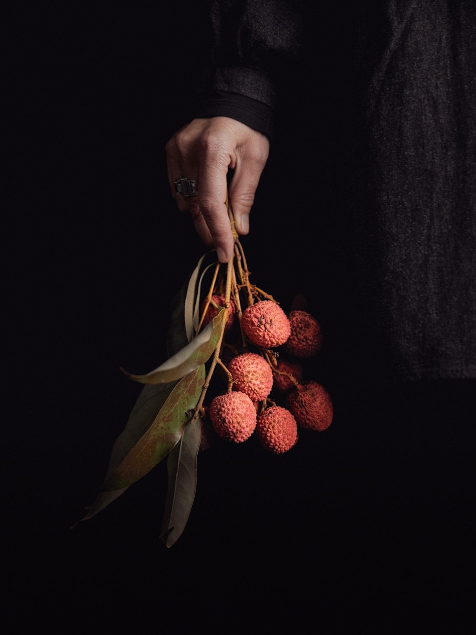 Eric Fenot photographe du magazine 180º Main qui tien un bouquet de litchies sur fond noir. Fhmt photo agent d'auteurs culinaire